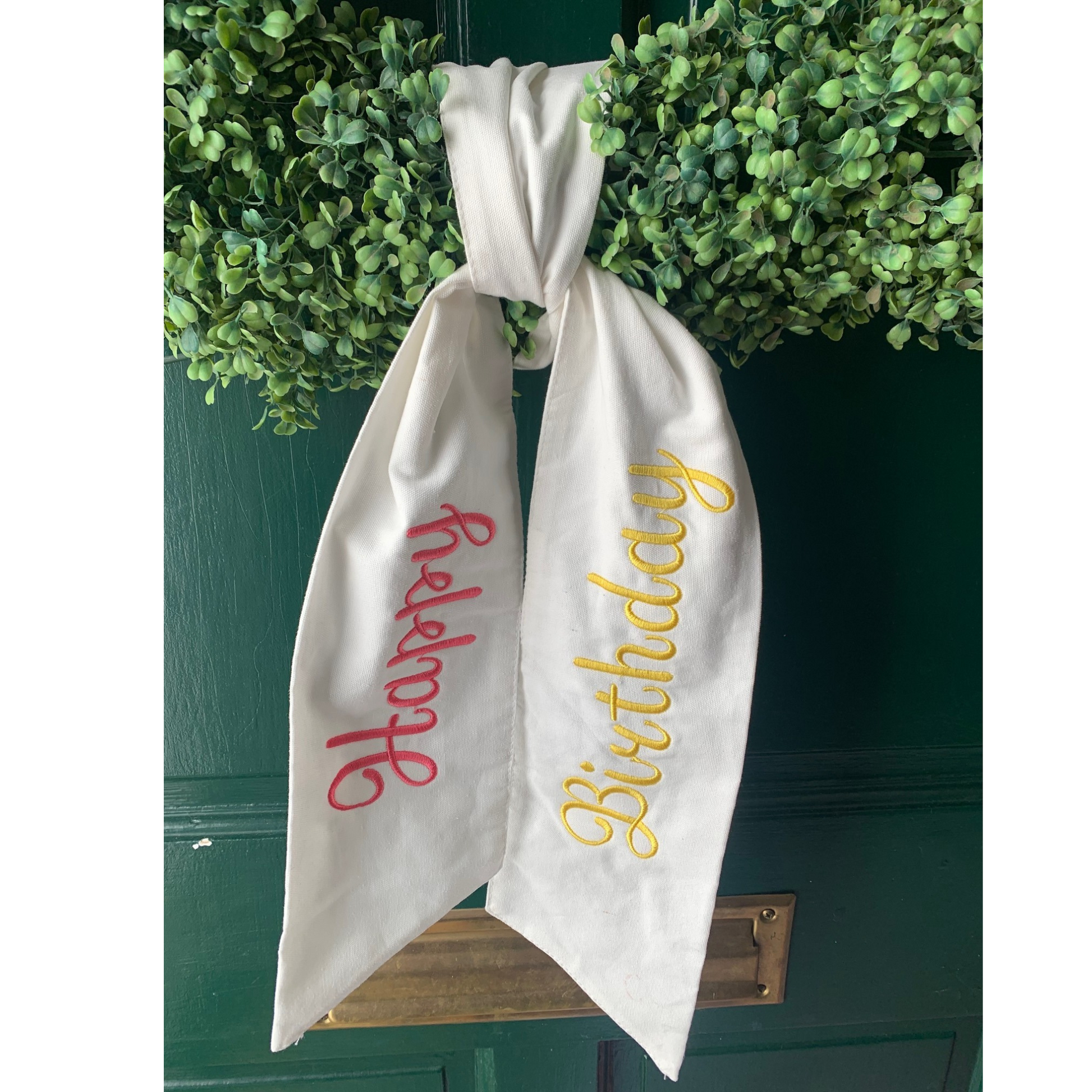 The word 'Birthday' embroidered in yellow and 'Happy' embroidered in yellow on a wreath sash.