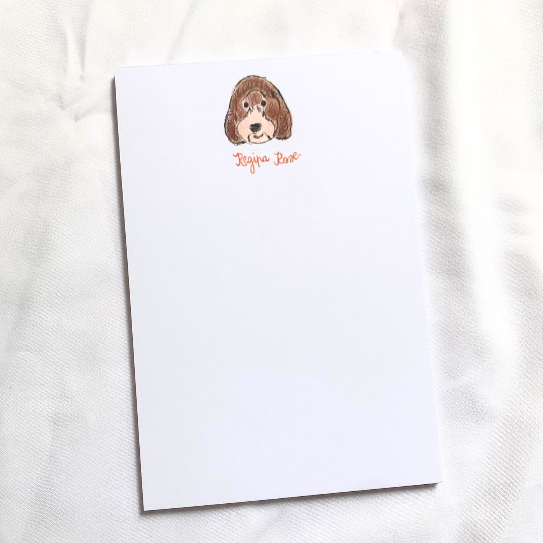 A notepad with an illustration of a cavapoo dog's face in the top left corner, labeled 'Regina Rose'. Regina Rose is the St. Mary's Hyde Park therapy dog. 